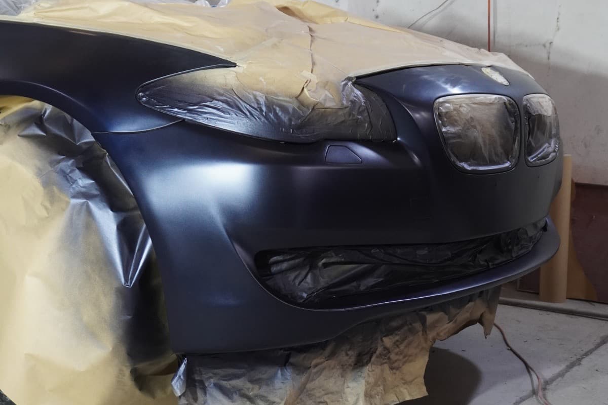 Defensa delantera en proceso de pintura automotriz con enmascarado profesional antes del acabado final